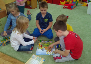 Dzieci grają na dywanie w grę planszową "Smoki".